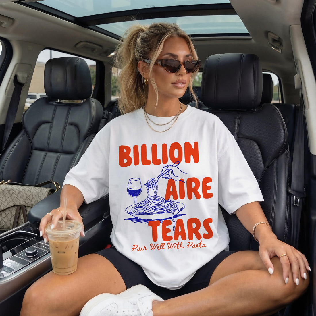 Woman in white t-shirt with &amp;quot;Billionaire Tears Pair Well With Pasta&amp;quot; graphic, sitting in a car.