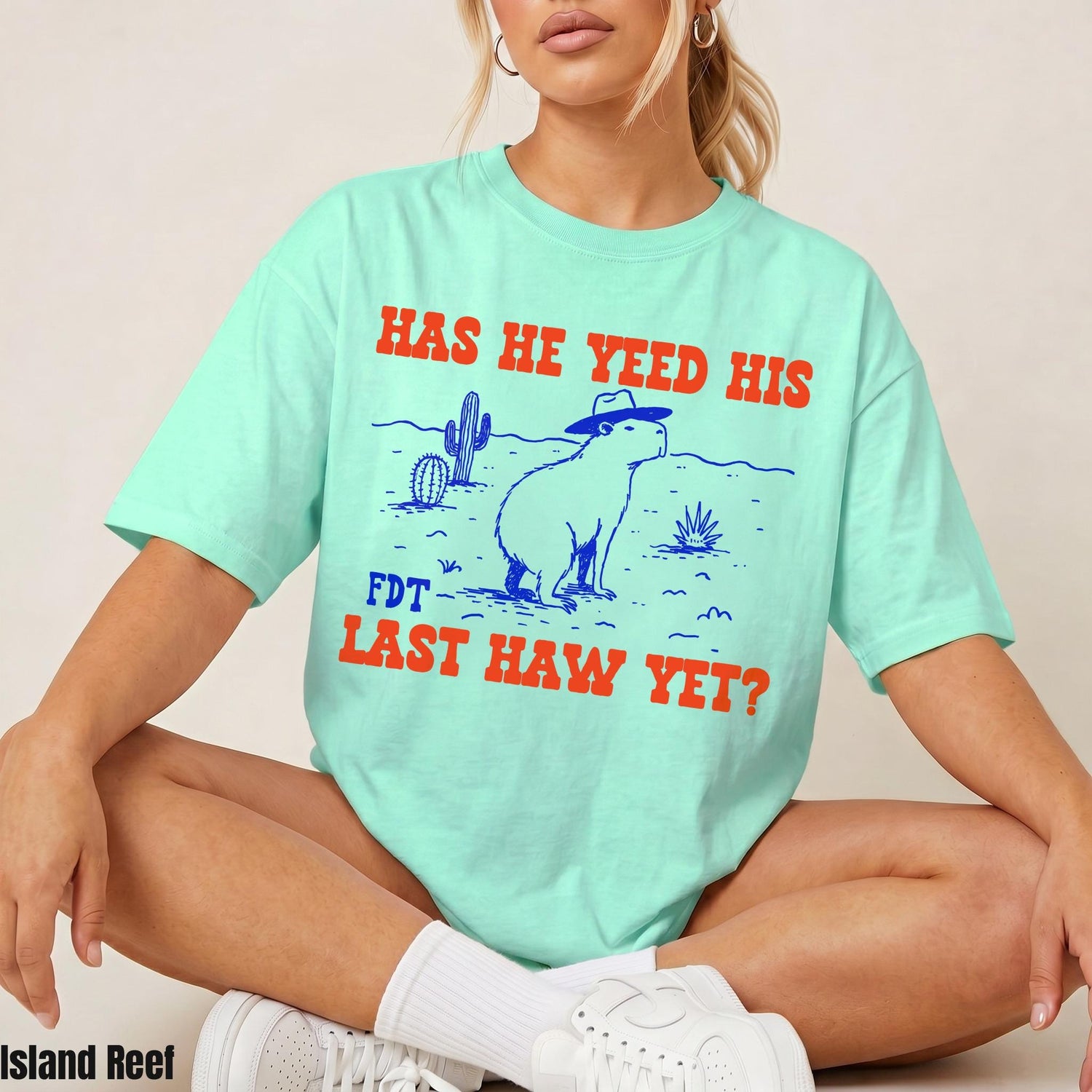Mint green t-shirt with a desert scene and capybara graphic, reading &amp;quot;HAS HE YEED HIS FDT LAST HAW YET?&amp;quot;.