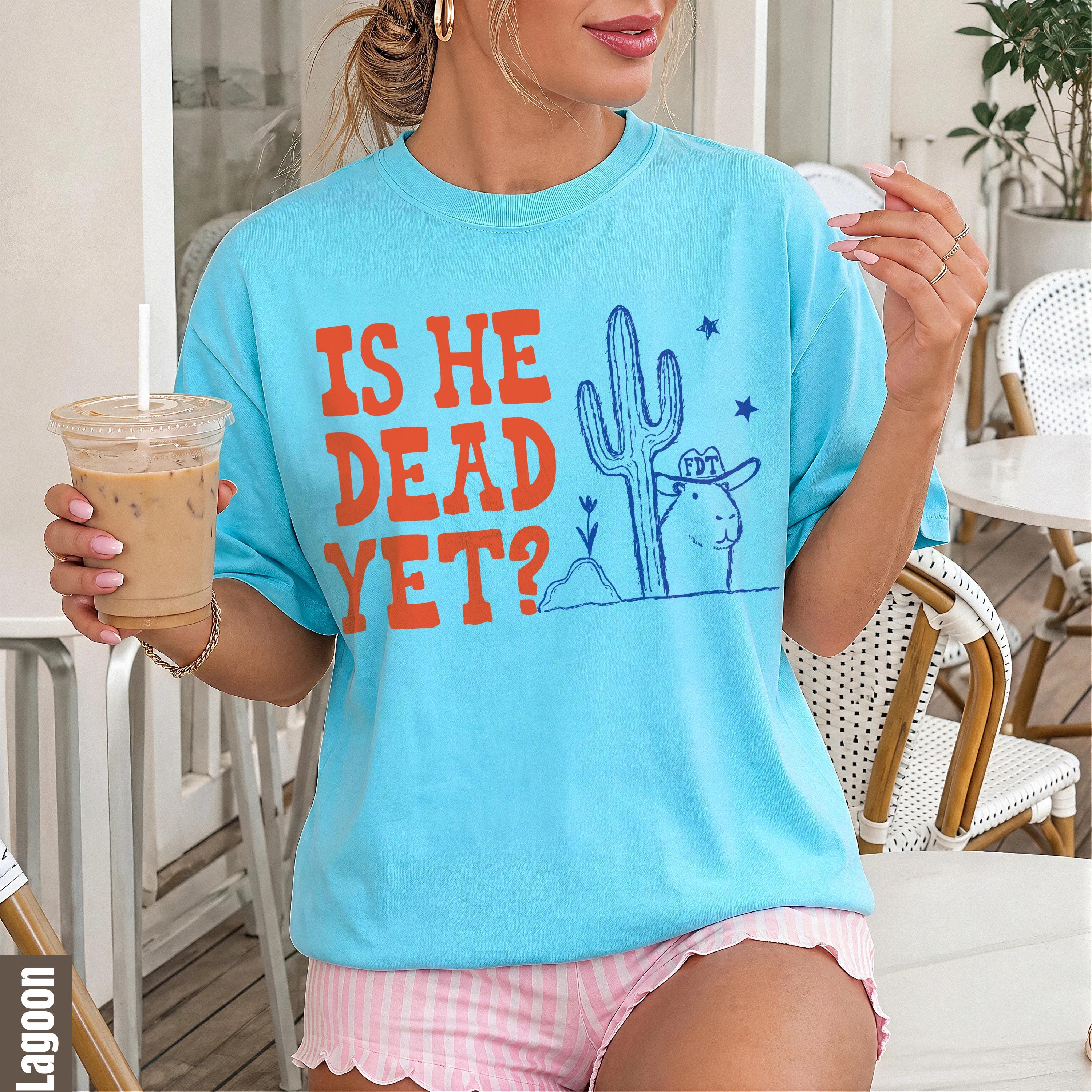 Light blue t-shirt with text &amp;quot;IS HE DEAD YET?&amp;quot; and desert graphic.