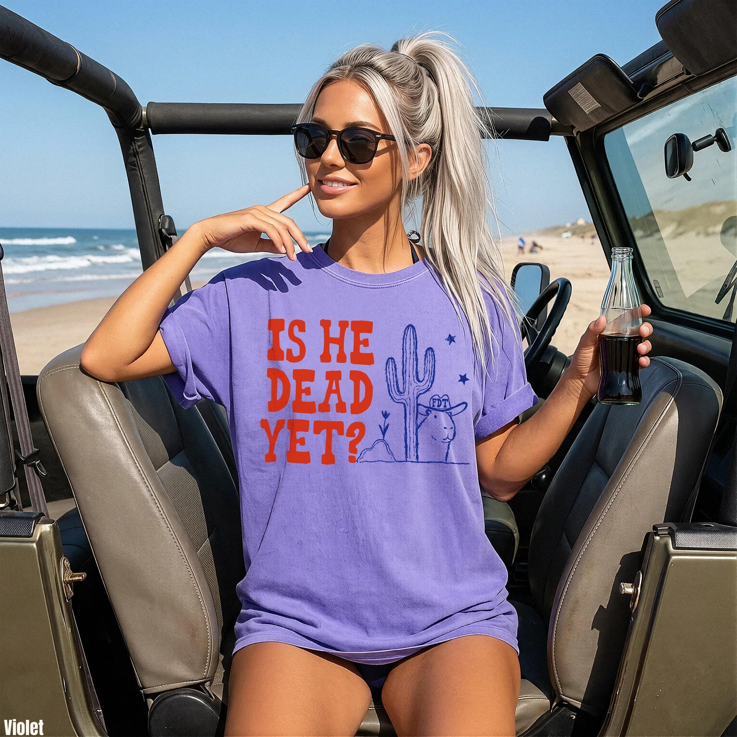 Woman wearing purple shirt with text &amp;quot;IS HE DEAD YET?&amp;quot; and desert graphic.