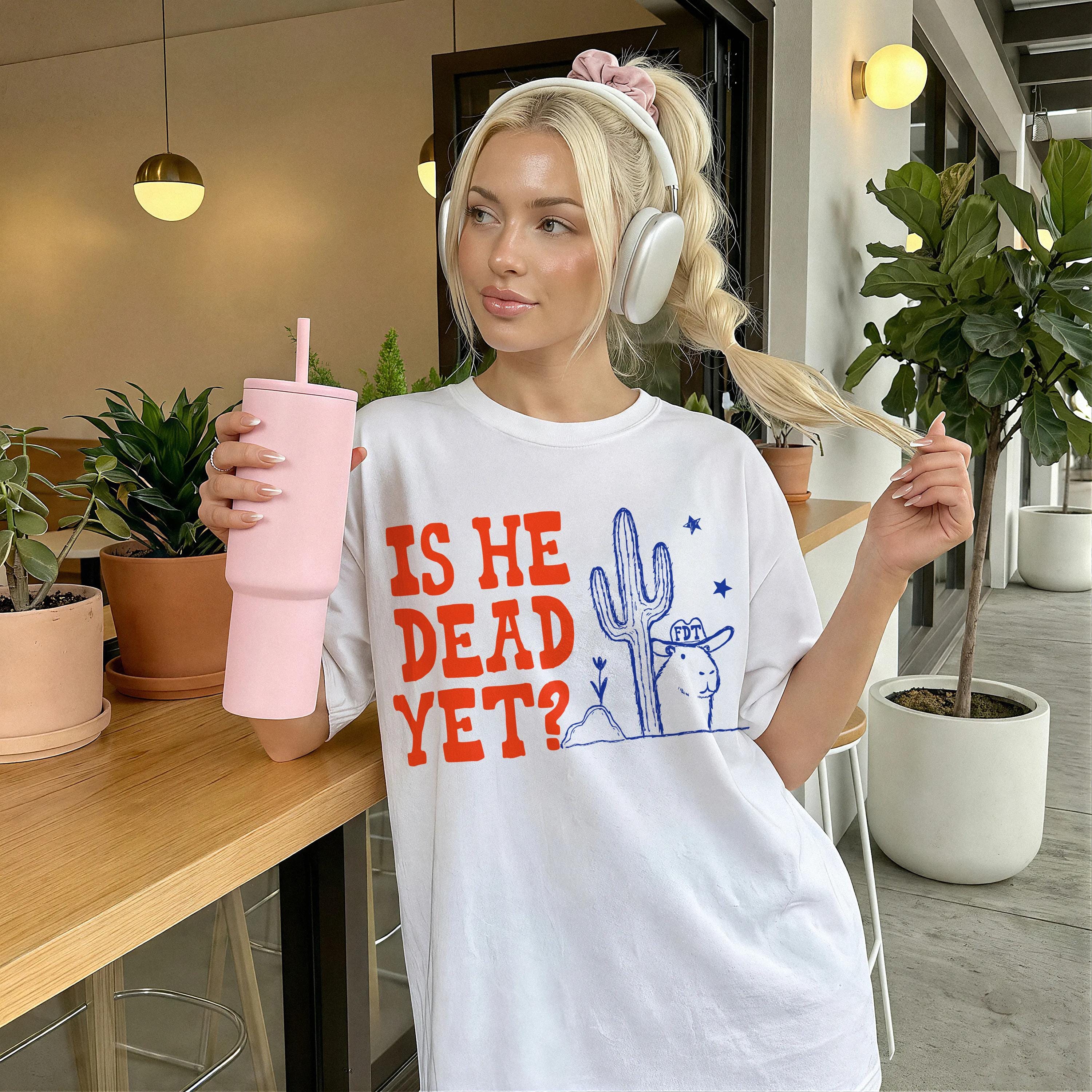 White t-shirt with graphic text &amp;quot;IS HE DEAD YET?&amp;quot; and desert imagery.