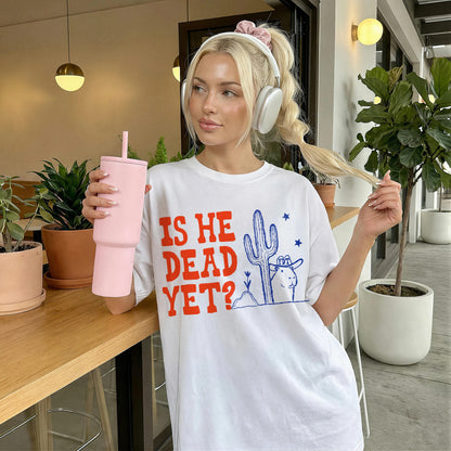 White t-shirt with graphic text &amp;quot;IS HE DEAD YET?&amp;quot; and desert imagery.