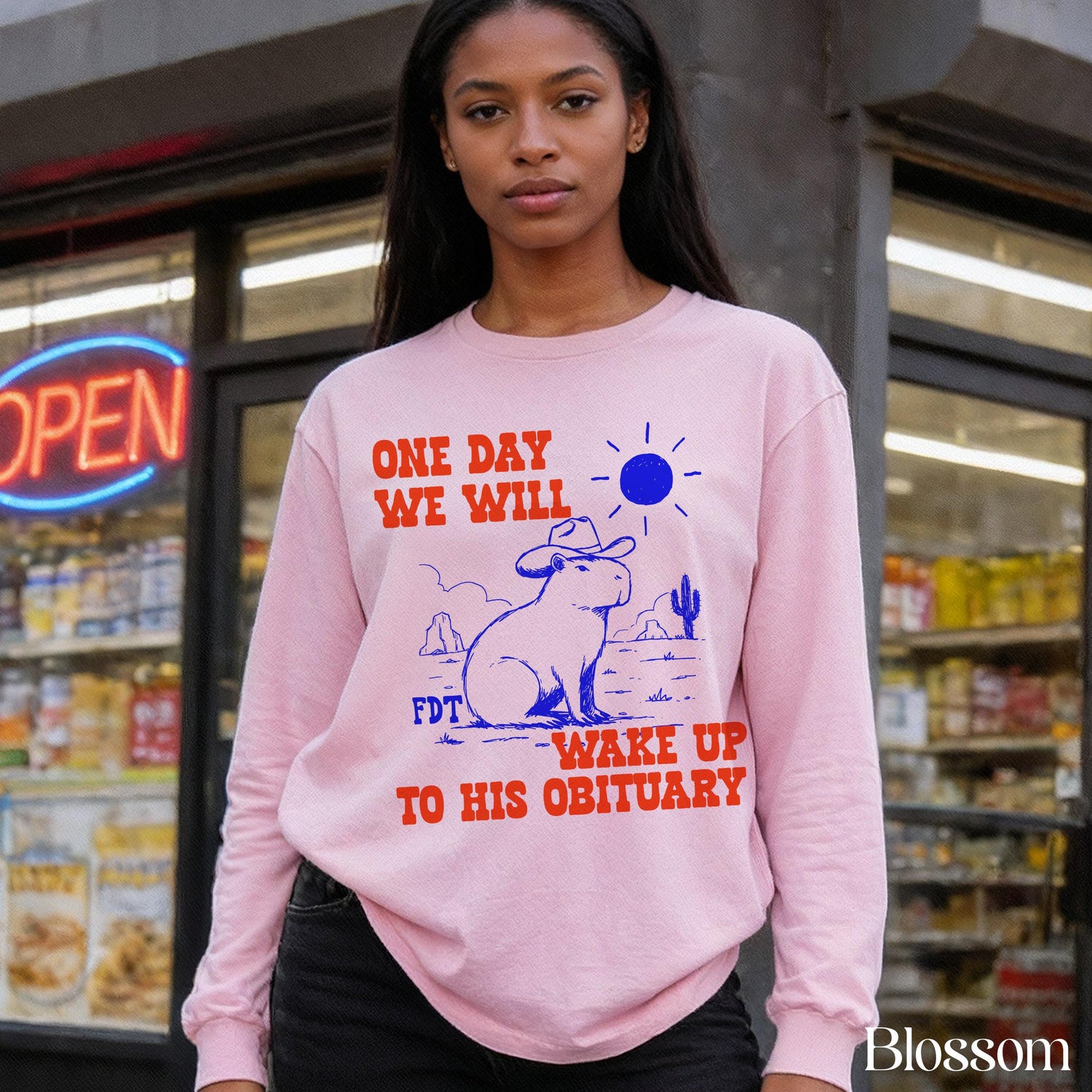 Pink sweatshirt with capybara graphic and text &amp;quot;ONE DAY WE WILL WAKE UP TO HIS OBITUARY&amp;quot;.