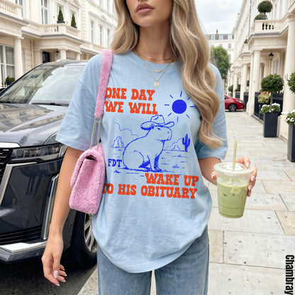 Light blue t-shirt with capybara wearing a hat graphic and &amp;quot;ONE DAY WE WILL WAKE UP TO HIS OBITUARY&amp;quot; text.