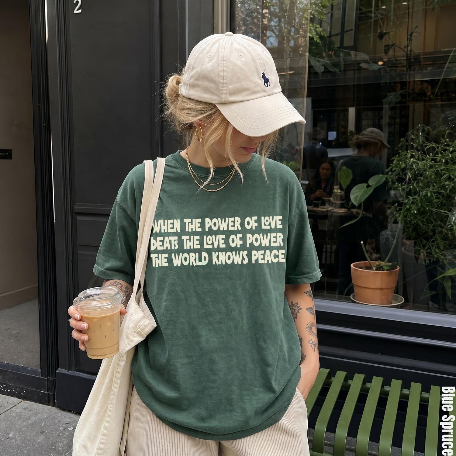 Woman in dark green t-shirt with text &amp;quot;When the power of love...&amp;quot; holding a coffee.