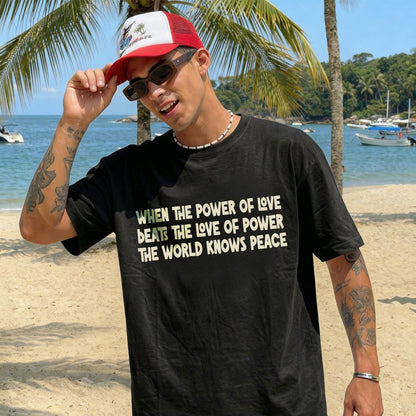 Man in black t-shirt with text, on a beach with palm trees and boats.