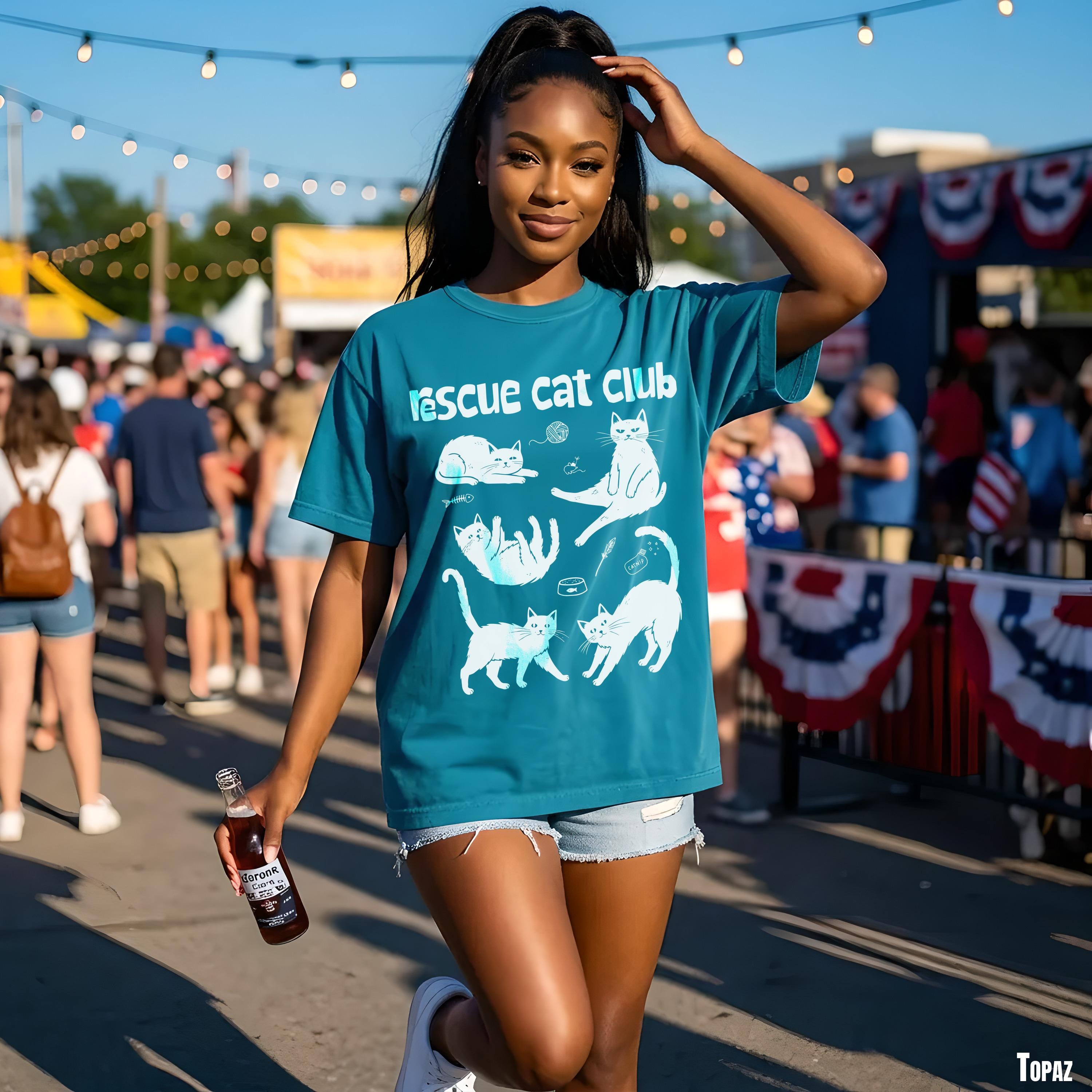 Woman in teal t-shirt with white cat illustrations holds a bottle.