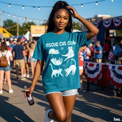Woman in teal t-shirt with white cat illustrations holds a bottle.