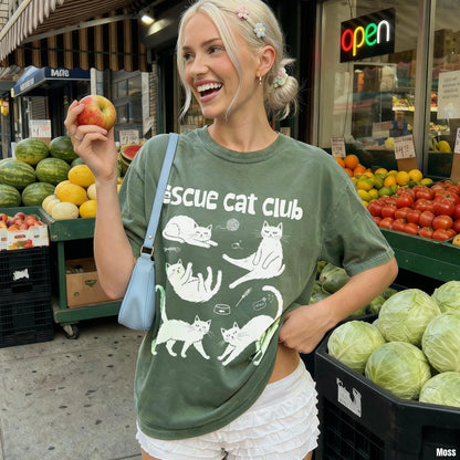 Woman in green &amp;quot;Rescue Cat Club&amp;quot; t-shirt holding apple outside market.