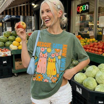 Woman in green t-shirt with &amp;quot;Rescue Cats Who&amp;quot; text and colorful cats, holding an apple.