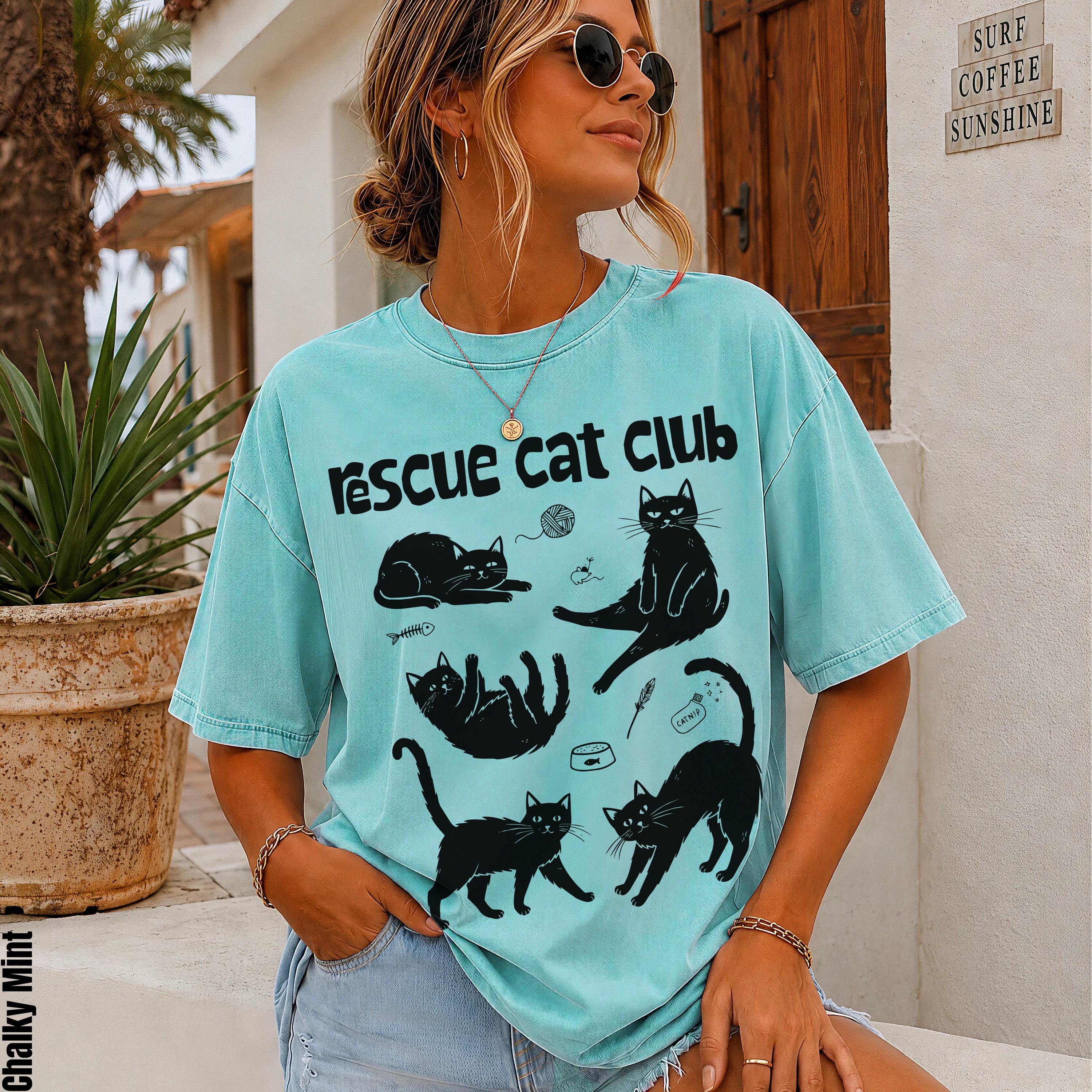 Woman wearing a teal t-shirt with cartoon black cats and &amp;quot;Rescue Cat Club&amp;quot; text.