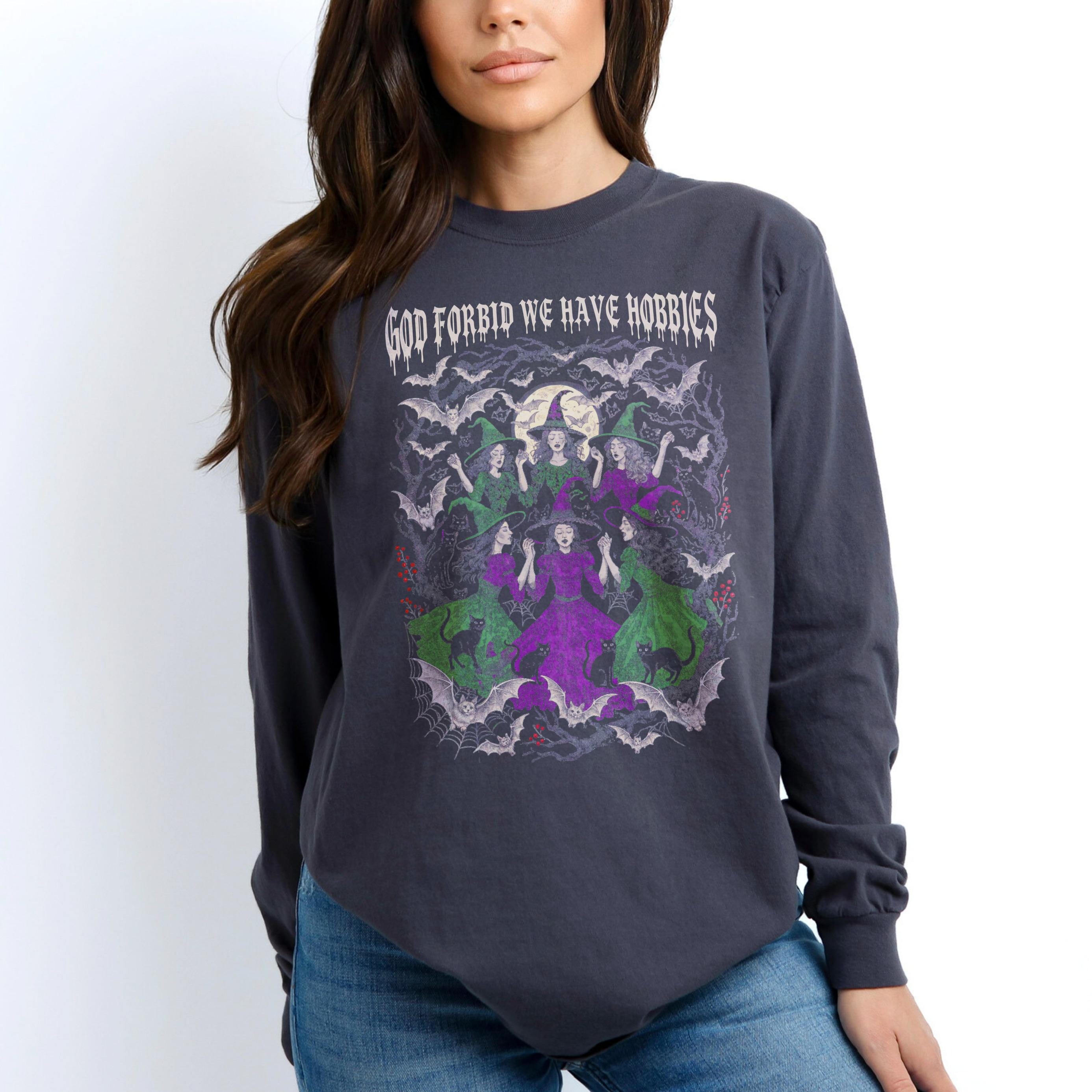 Long sleeve t-shirt with graphic of witches, cats, bats, and moon. Text reads &amp;quot;God forbid we have hobbies&amp;quot;.