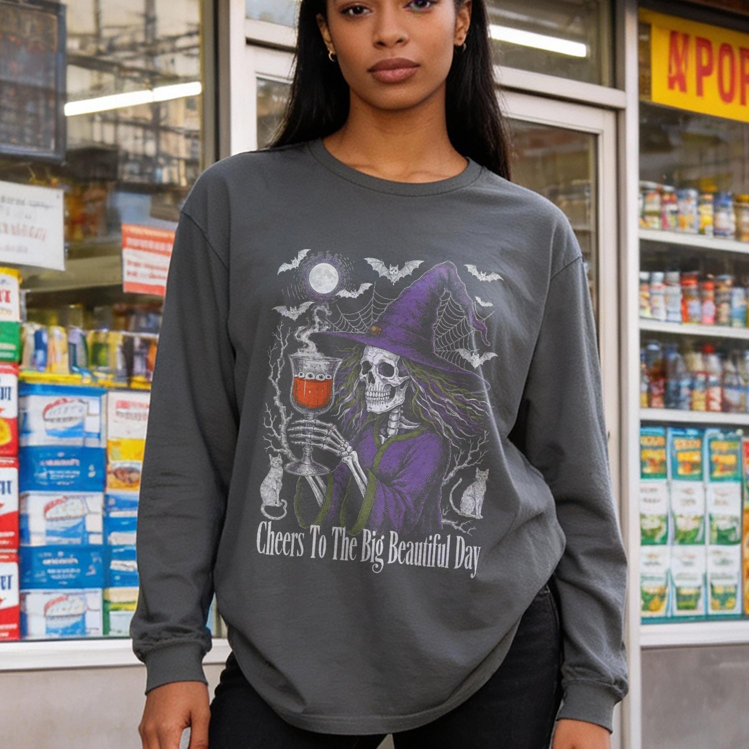 Skeleton witch holding a drink on a dark gray long-sleeved shirt.