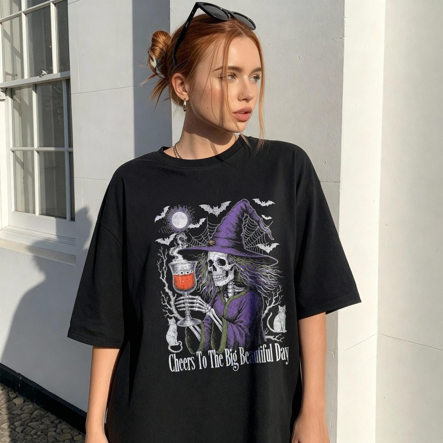 Black t-shirt with skeleton witch graphic and text &amp;quot;Cheers To The Big Beautiful Day&amp;quot;.