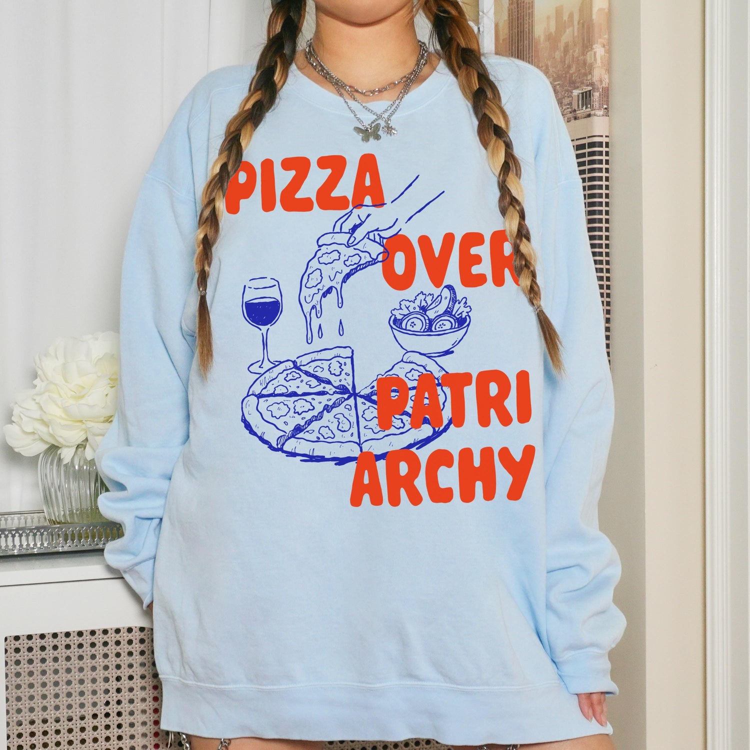Light blue sweatshirt with orange &amp;quot;Pizza Over Patriarchy&amp;quot; graphic featuring pizza slice and salad.