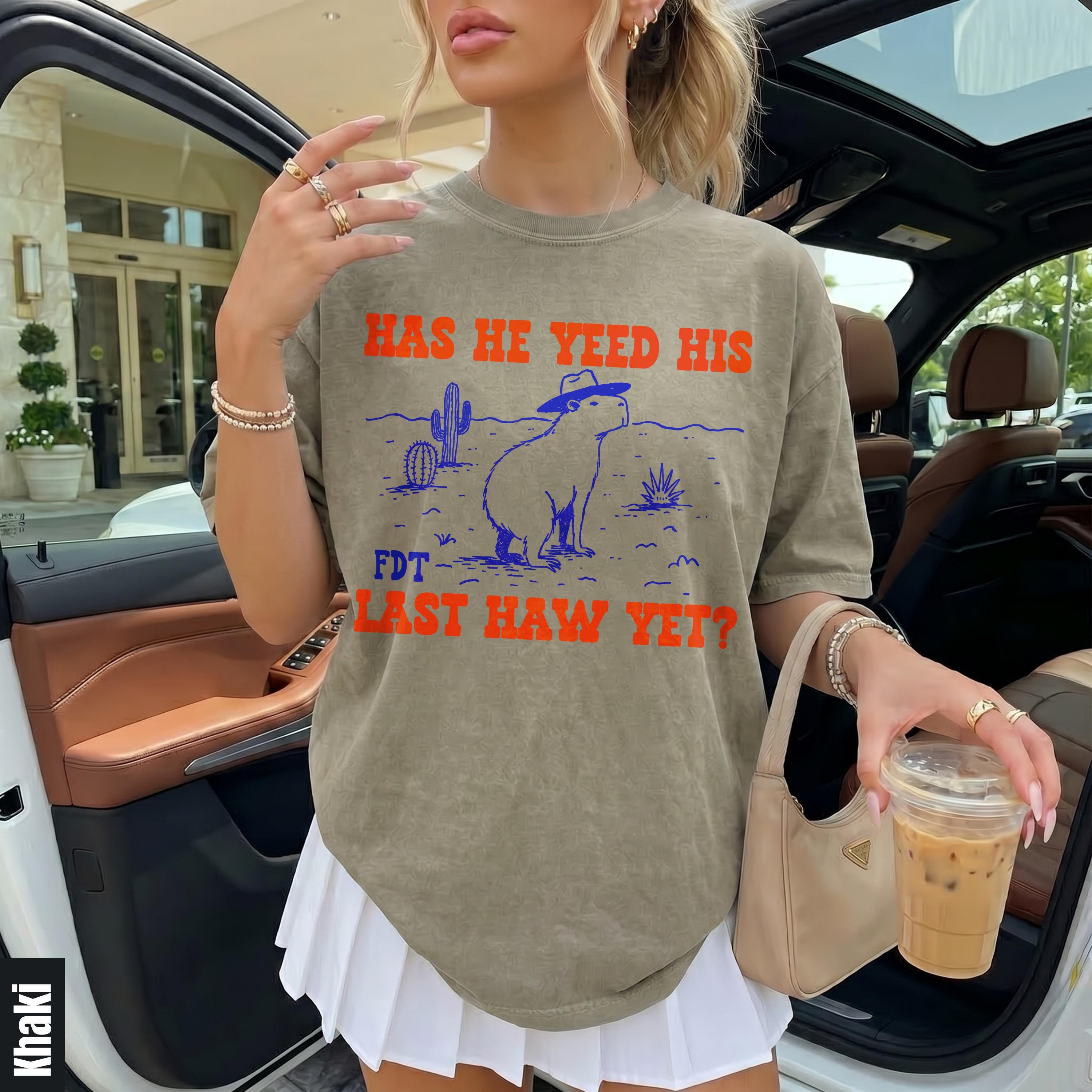 Khaki t-shirt with a cowboy capybara graphic and text &amp;quot;HAS HE YEED HIS FDT LAST HAW YET?&amp;quot;.