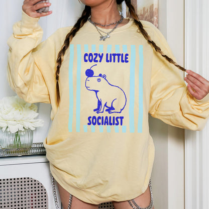 Yellow sweatshirt with blue capybara graphic and text &amp;quot;Cozy Little Socialist&amp;quot;.