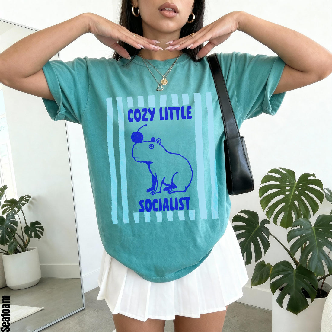 Teal t-shirt with blue capybara graphic and text &amp;quot;Cozy Little Socialist&amp;quot;.