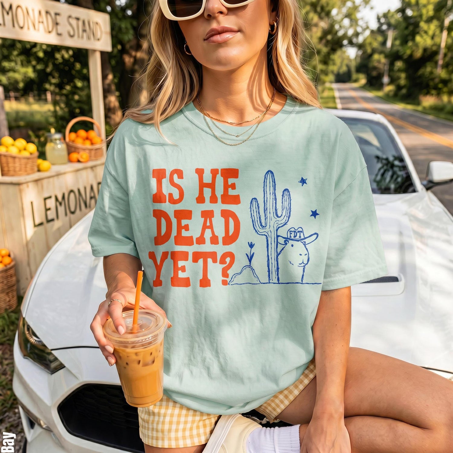 Light blue t-shirt with orange text &amp;quot;IS HE DEAD YET?&amp;quot; and desert graphic.