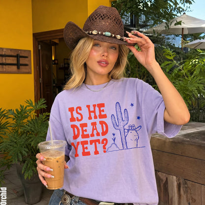 Woman wearing lavender t-shirt with &amp;quot;IS HE DEAD YET?&amp;quot; and desert graphic.
