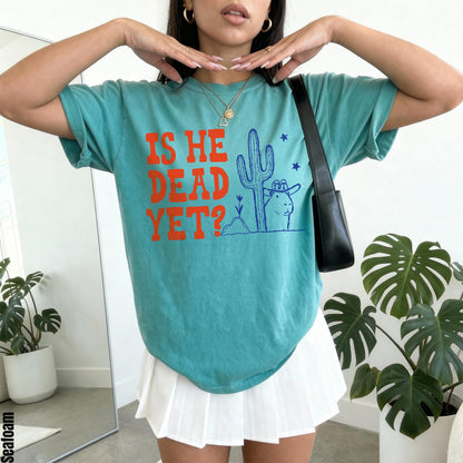 Teal t-shirt with orange text &amp;quot;IS HE DEAD YET?&amp;quot; and a cartoon desert design.