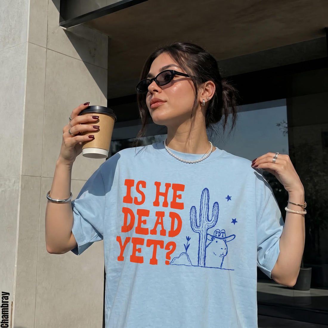 Light blue t-shirt with orange text &amp;quot;IS HE DEAD YET?&amp;quot; and a blue drawing.