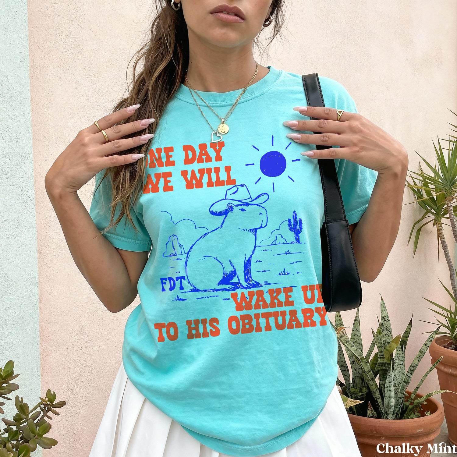 Teal t-shirt with orange text &amp;quot;ONE DAY WE WILL WAKE UP TO HIS OBITUARY.&amp;quot;