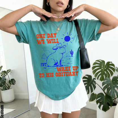 Teal t-shirt with &amp;quot;ONE DAY WE WILL WAKE UP TO HIS OBITUARY&amp;quot; and capybara graphic.