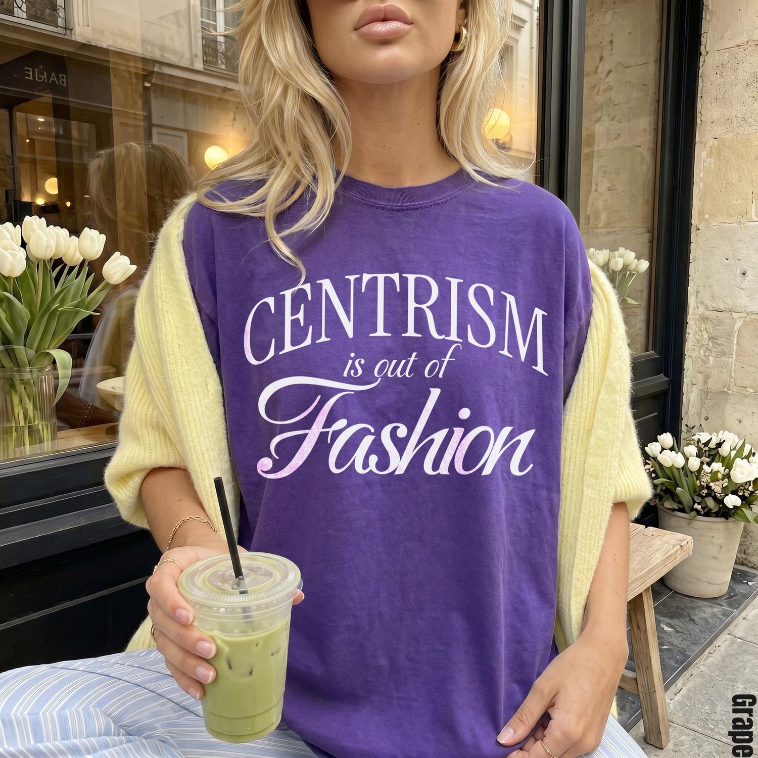 Purple t-shirt with &amp;quot;CENTRISM is out of Fashion&amp;quot; text, held iced drink.