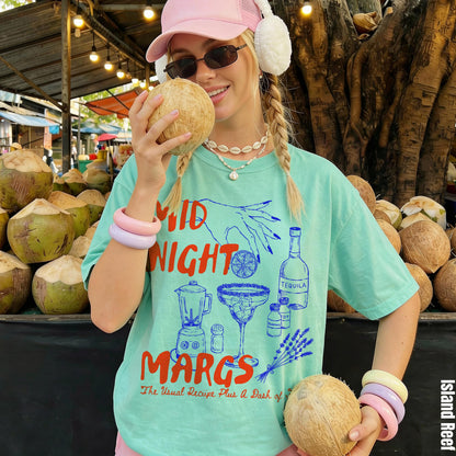 Woman in mint green t-shirt with &amp;quot;Midnight Margs&amp;quot; print holding a coconut.