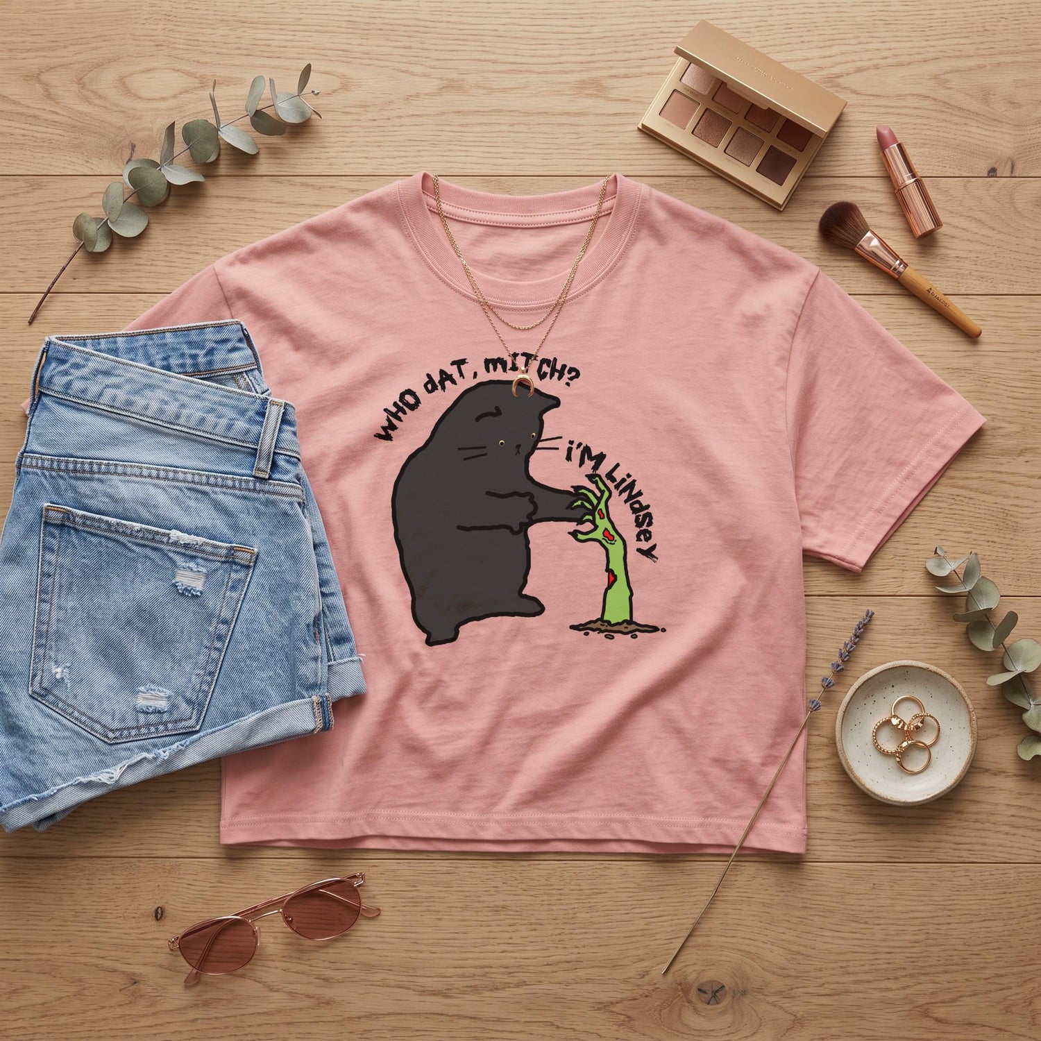Pink t-shirt featuring a black cat and zombie hand graphic with text.