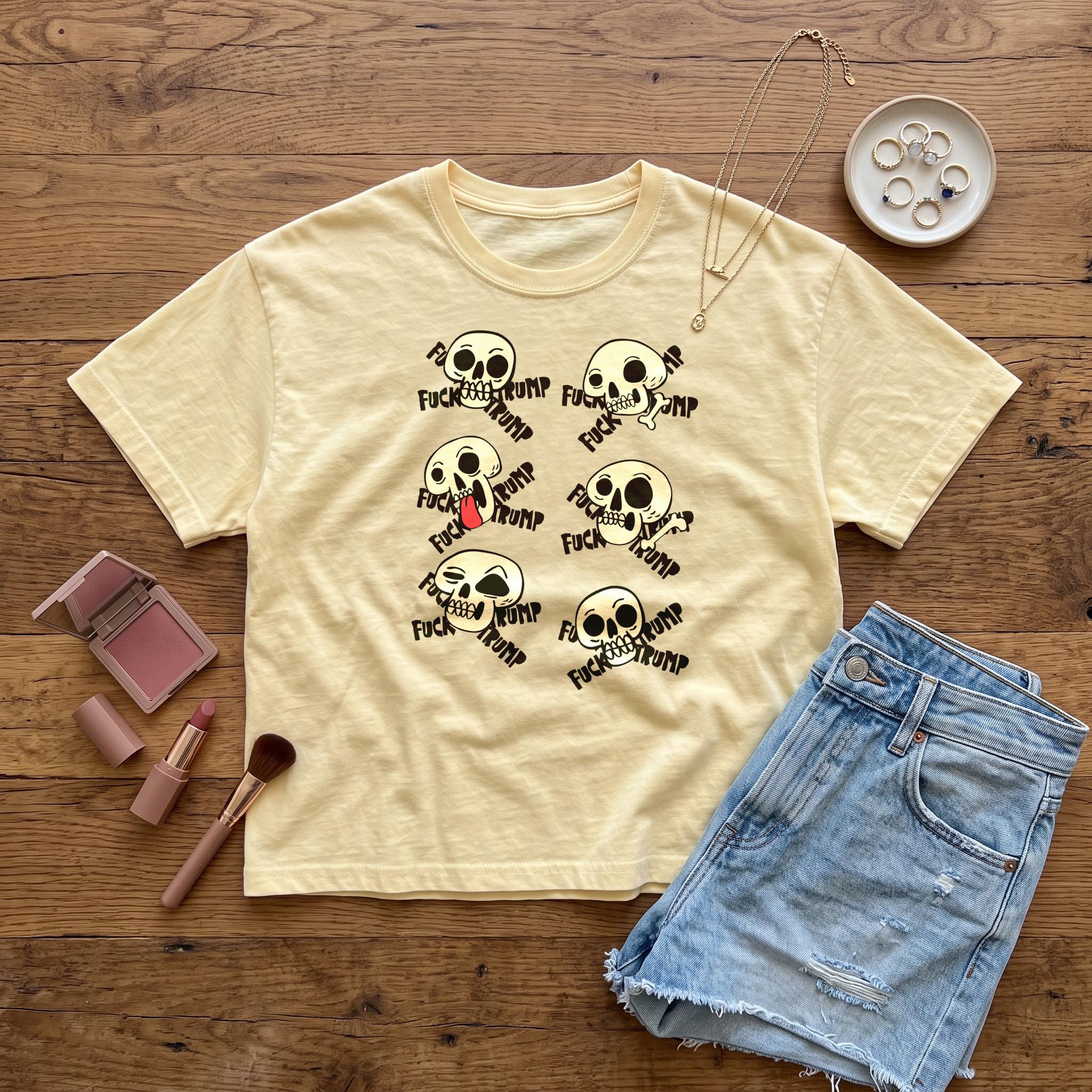 Light yellow t-shirt with multiple skull graphics saying &amp;quot;FUCK TRUMP&amp;quot; displayed on a wooden surface.