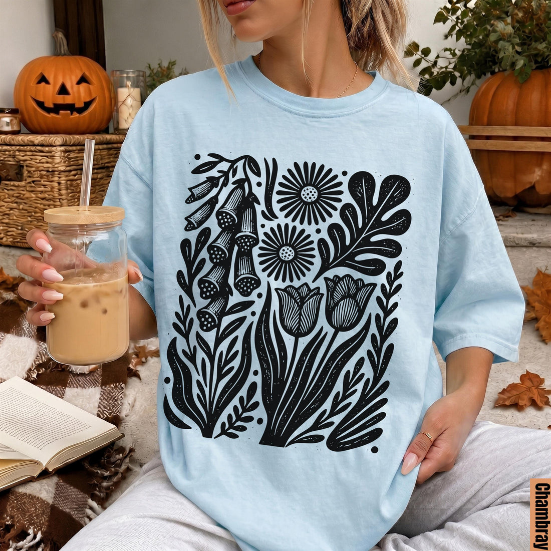 Light blue t-shirt with black floral and leaf print, held by a person with a drink.