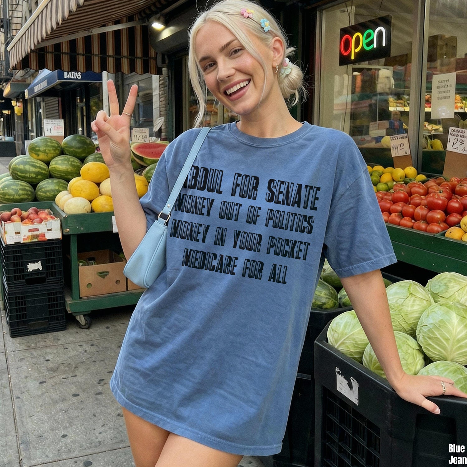 Woman in blue t-shirt with &amp;quot;Boul for Senate&amp;quot; text, standing by produce stand.