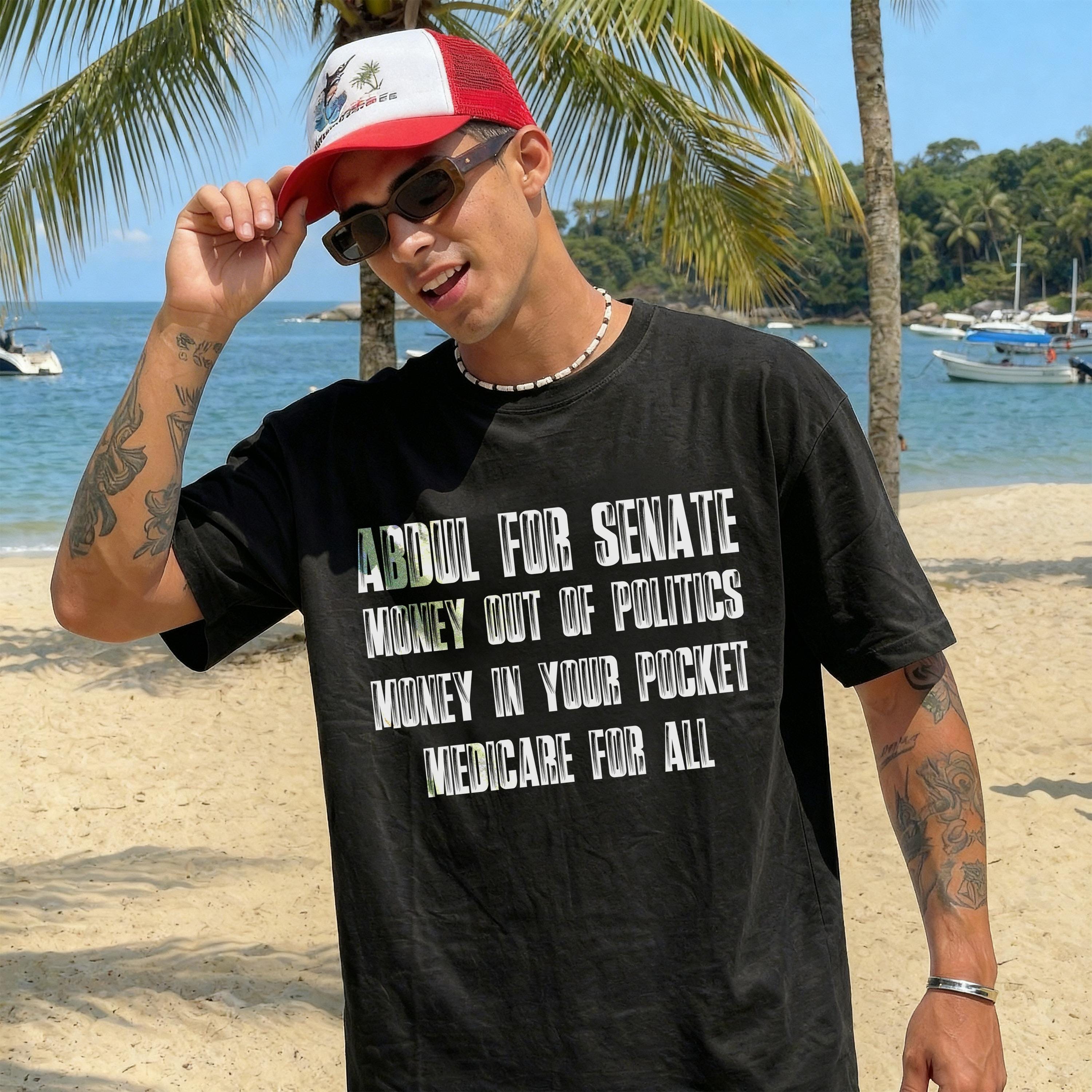 Man on beach wears black t-shirt with &amp;quot;Abdul for Senate&amp;quot; and political slogans.