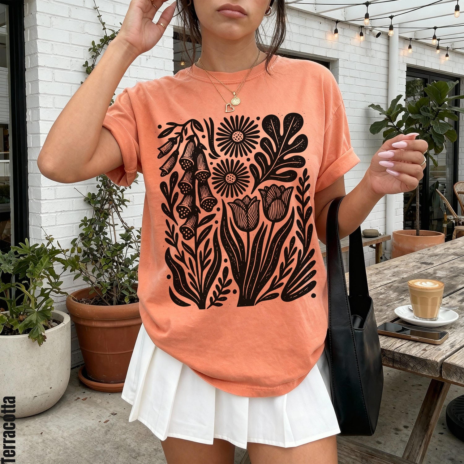 Peach t-shirt with black floral linocut design, white pleated skirt, black bag. &amp;quot;Terracotta&amp;quot; text.