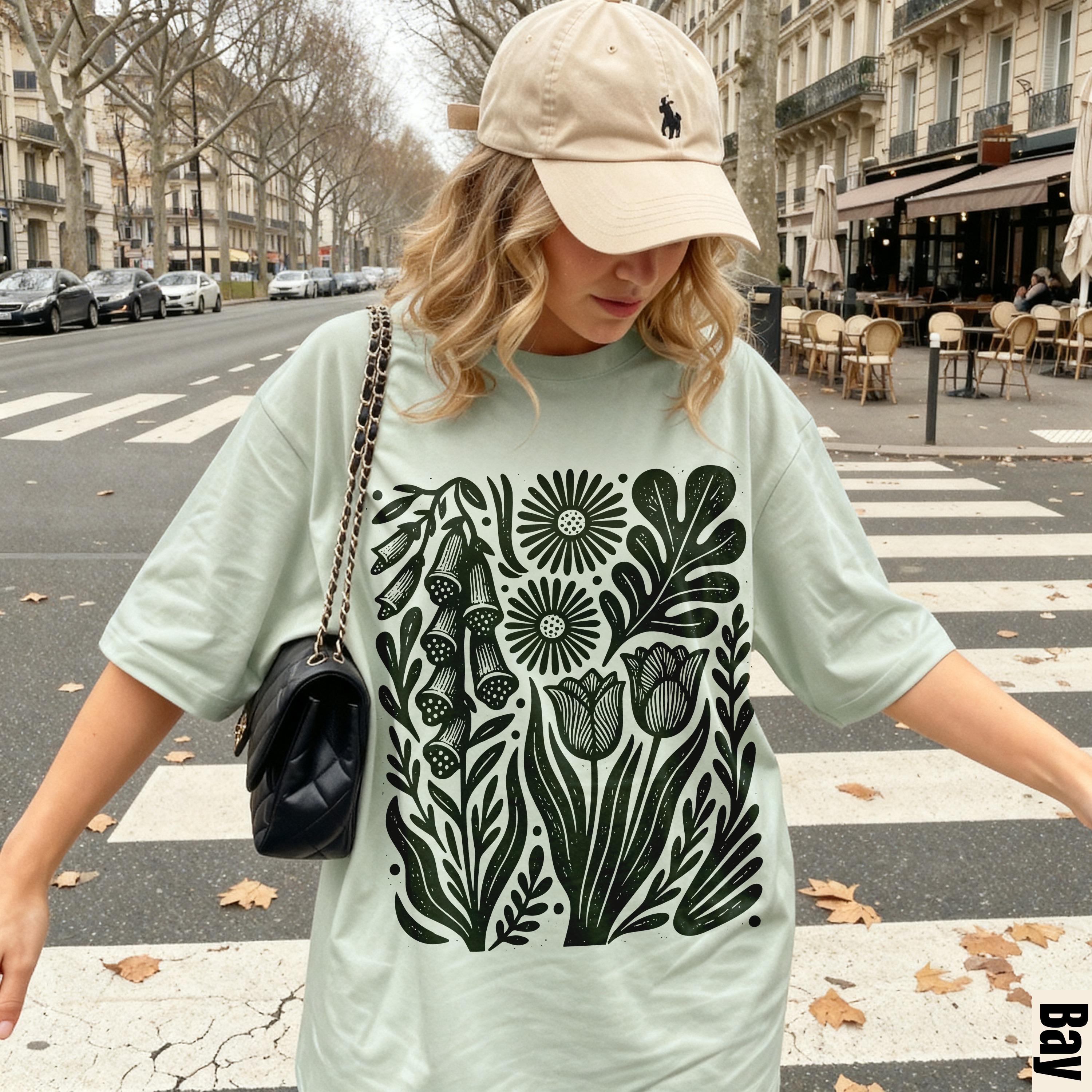 Woman wearing light green t-shirt with black floral print, standing on crosswalk.