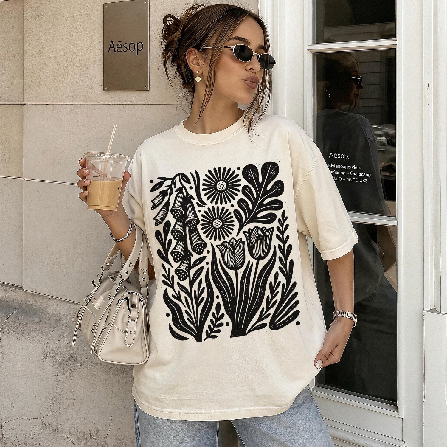 Cream t-shirt with black floral print, worn by a woman holding iced coffee.