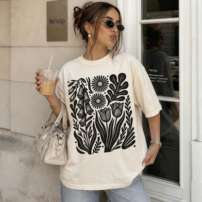 Cream t-shirt with black floral print, worn by a woman holding iced coffee.