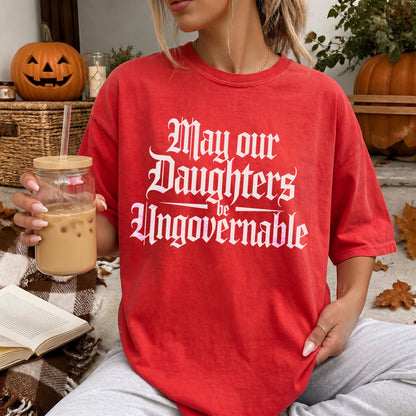 Red t-shirt with white text &amp;quot;May our Daughters be Ungovernable&amp;quot; and autumn decorations.