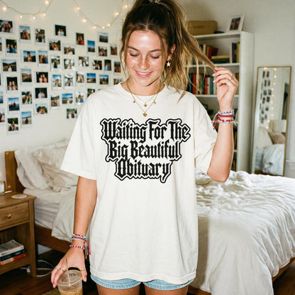 Cream t-shirt with black gothic text &amp;quot;Waiting For The Big Beautiful Obituary&amp;quot;.