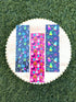 May include: Three rectangular bookmarks featuring vibrant patterns. The left bookmark has a dark background with neon palm trees and ice cream cones. The center bookmark has a bright pink background with orange pumpkins, white ghosts, and blue skulls. The right bookmark has a dark background with neon ghosts, spiderwebs, and bats.