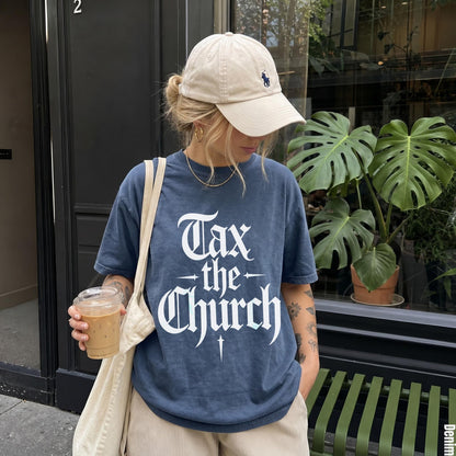 Woman in blue t-shirt with &amp;quot;Tax the Church&amp;quot; graphic holds iced coffee.