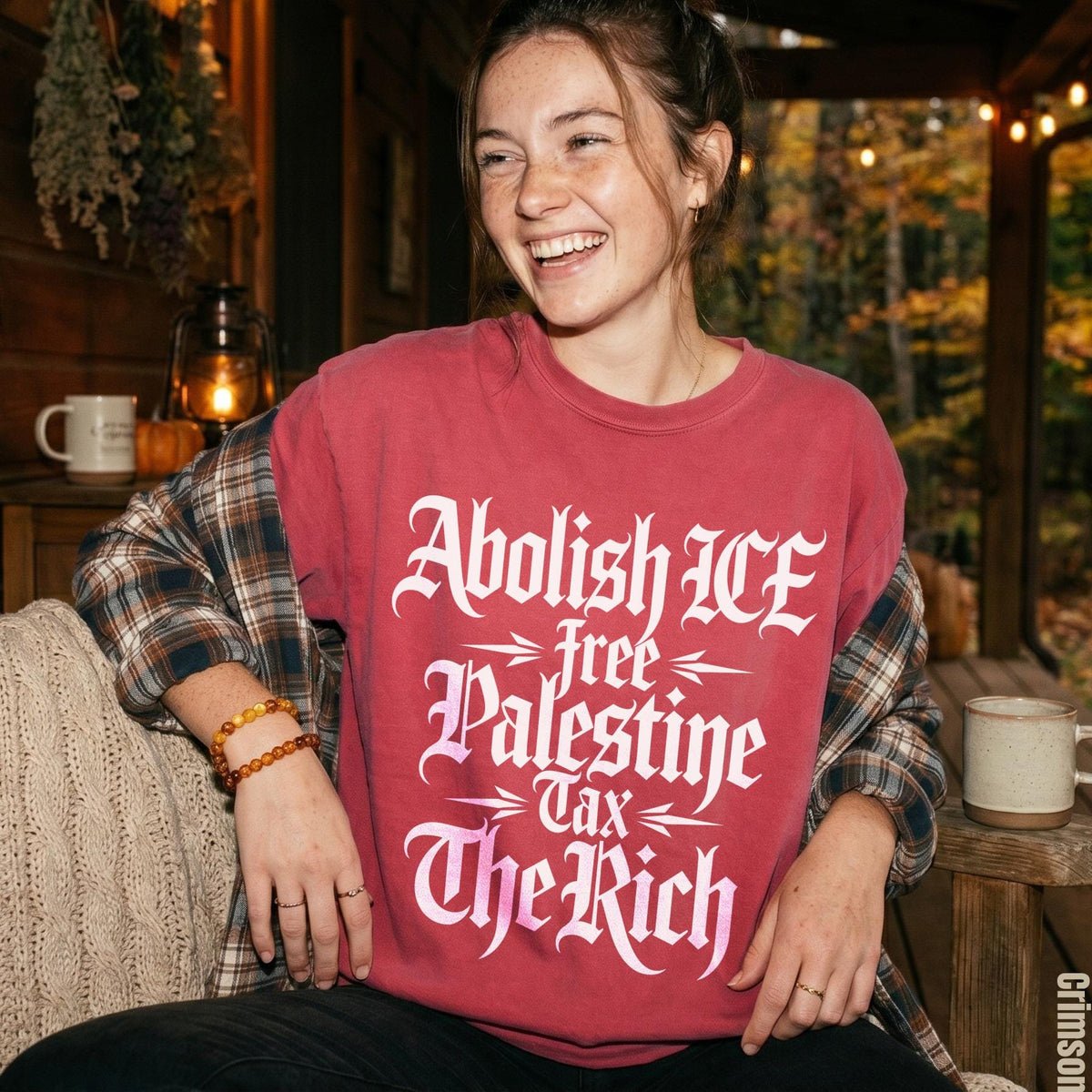 Woman wearing a maroon shirt with white text: Abolish ICE, Free Palestine, Tax The Rich.