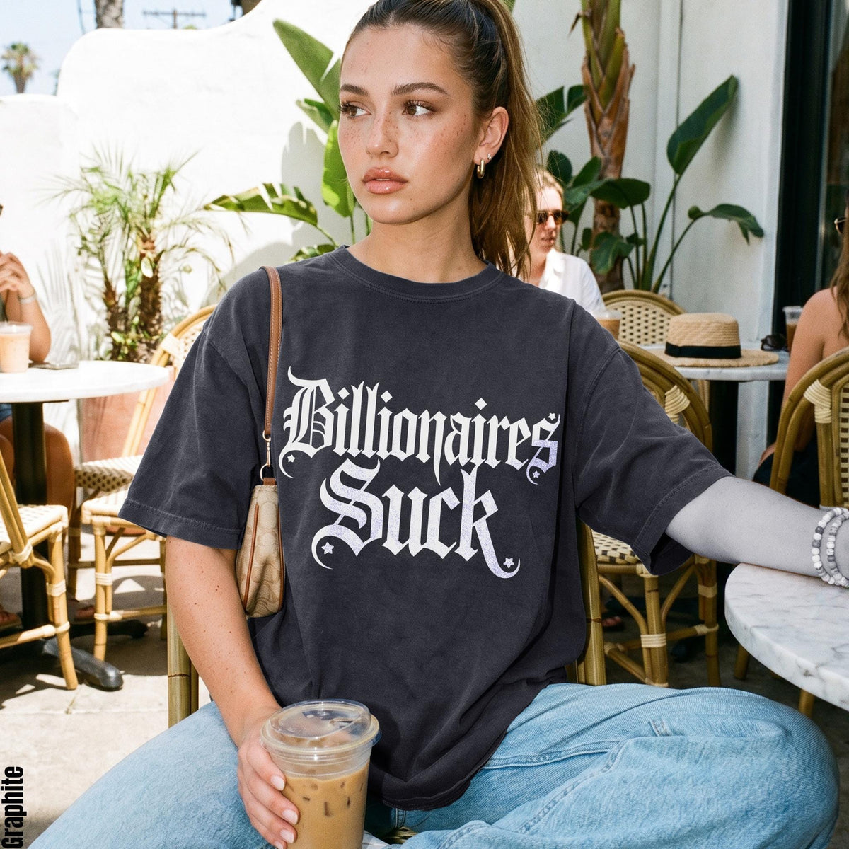 Woman wearing a dark gray t-shirt with &amp;quot;Billionaires Suck&amp;quot; text, holding iced coffee.