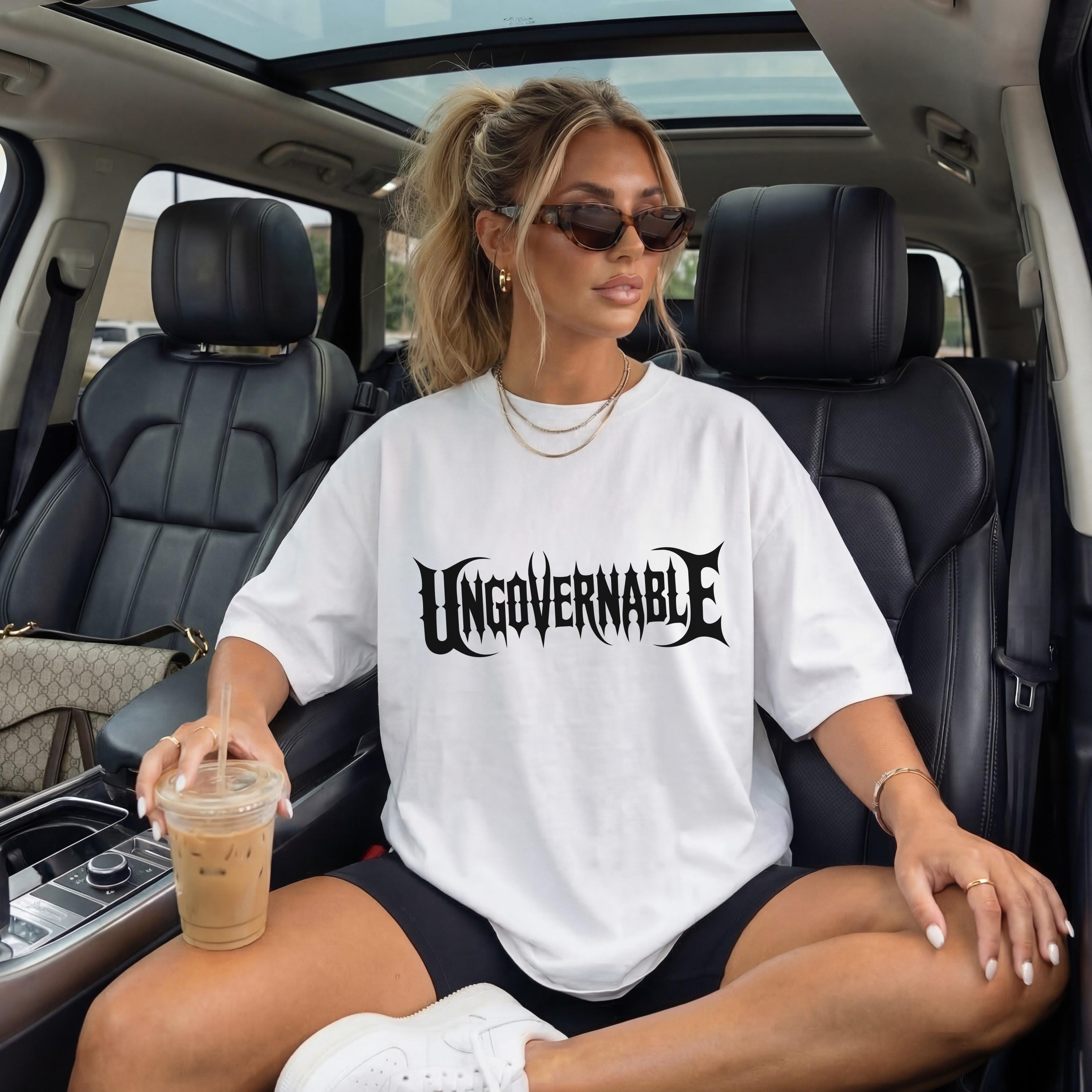 Woman in white t-shirt with &amp;quot;UNGVVERNABLE&amp;quot; graphic sitting in car.