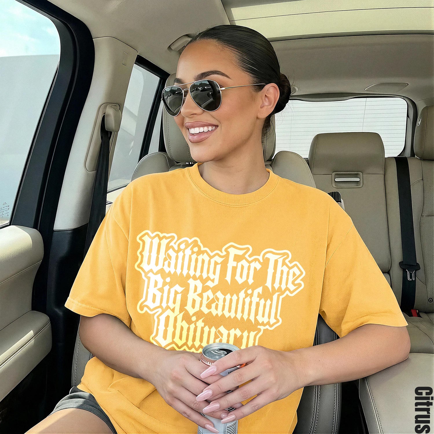 Woman in yellow t-shirt with &amp;quot;Waiting For The Big Beautiful Obituary&amp;quot; text holds a can.