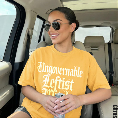 Woman in yellow shirt with &amp;quot;Ungovernable Leftist&amp;quot; text, holding a can in a car.