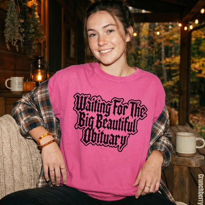 Pink t-shirt with black text &amp;quot;Waiting For The Big Beautiful Obituary.&amp;quot;