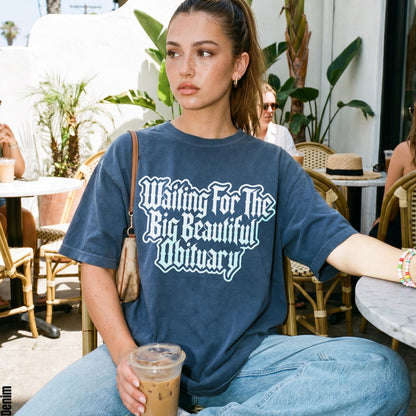 Woman wearing a dark blue t-shirt with &amp;quot;Waiting For The Big Beautiful Obituary&amp;quot; text.